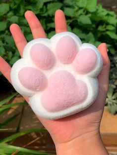 a person holding up a pink and white paw toy in front of some green plants