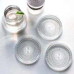 four glass coasters with the letter n on them and a bottle of alcohol in the background