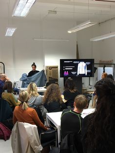 a group of people sitting at tables in front of a projector screen with clothes on it