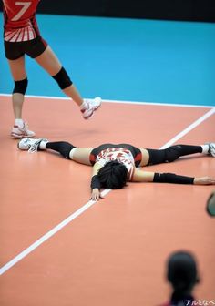 a woman laying on the ground in front of a tennis ball while another person stands behind her