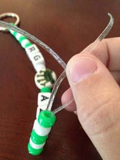 a hand holding a green and white beaded keychain with letters on it