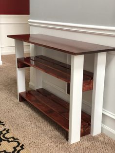 a wooden table with two shelves on the bottom and one shelf below it, against a white wall