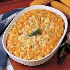 a casserole dish filled with macaroni and cheese next to corn on the cob