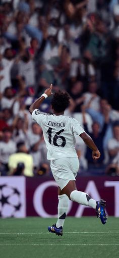 a soccer player is running on the field with his arms in the air as people watch from the stands