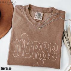 The Comfort Colors® Nurse Groovy Shirt is a retro-inspired tee that features the word "NURSE" in a playful, wavy outline font. This shirt makes a fantastic gift for registered nurses, nursing students, or anyone in the nursing profession. It's perfect for Nurse Appreciation events, graduation gifts, or simply as a stylish addition to any nurse's casual wardrobe. The Comfort Colors fabric offers a soft, lived-in feel, adding comfort to its unique, groovy design. Browse our collection and order yo Neuro Nurse Shirt, Nurse Tshirt Designs, Nurse Shirts Ideas, Outline Font, Nursing Student Shirts, Nursing Gifts, Groovy Shirt, Groovy Design, Student Shirt