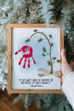 someone is holding up a handprinted christmas ornament in front of a tree