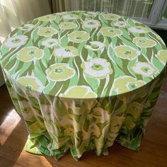 a round table with green and white flowers on it, in front of a window