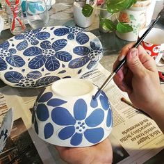 a person is painting a blue flower on a white bowl with a brush in their hand