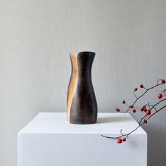 a wooden vase sitting on top of a white block next to a plant with red berries