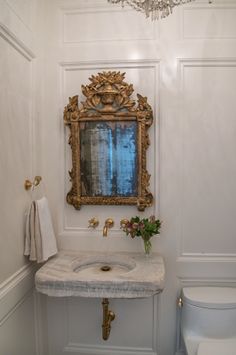 a bathroom with a sink, mirror and toilet in it's corner area next to a chandelier hanging from the ceiling