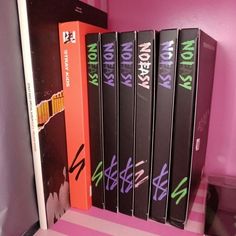 a row of books sitting on top of a pink shelf in front of a refrigerator