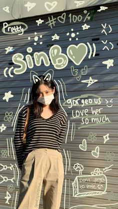 a woman wearing a face mask standing in front of a wall with graffiti on it