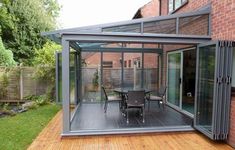 an enclosed patio with table and chairs in the back yard, next to a brick building