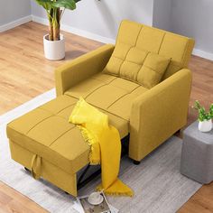 a living room with a yellow chair and footstool on the floor in front of a potted plant