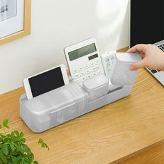 a person holding a remote control next to a cell phone and laptop on a desk