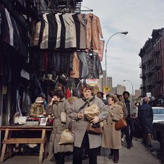 people are walking down the street in front of clothing racks and clothes hanging on poles