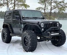 a black jeep is parked in the snow near some trees and water with it's lights on