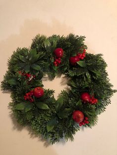 a green wreath with red berries and greenery hanging on the wall next to a white wall