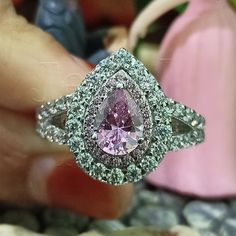 a close up of a person holding a ring with a pink diamond in the middle