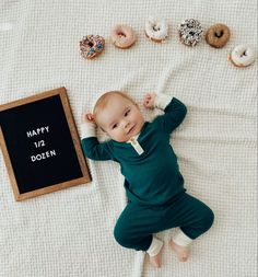 a baby laying on top of a bed next to doughnuts and a chalkboard