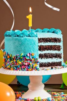 a blue birthday cake with sprinkles and a single lit candle on top