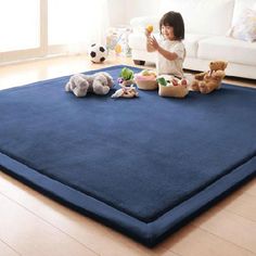 a child playing with stuffed animals on a blue rug in front of a white couch