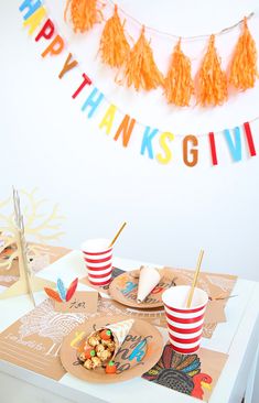 a table topped with paper plates and cups filled with food next to a happy thanksgiving banner