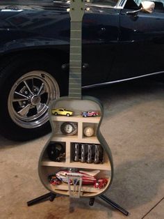 a guitar shaped toy sitting on top of a stand in front of a black car