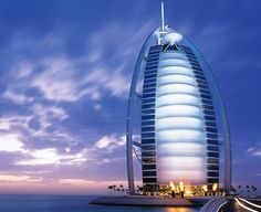 the burj building is lit up at night by the water's edge