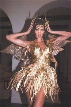 a woman in a gold dress with wings on her head and hands behind her head