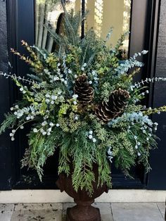 a planter with pine cones and greenery in front of a black door way