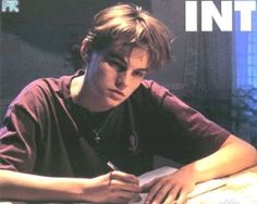 a young man sitting at a table writing on a piece of paper with a pen in his hand