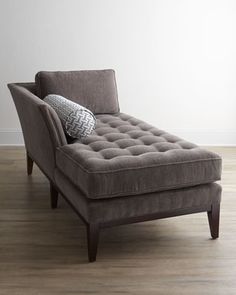 a gray chaise lounger sitting on top of a hard wood floor next to a white wall