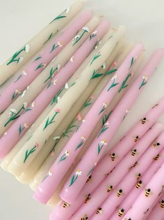 pink candles with white flowers and green leaves are lined up in a row on top of each other