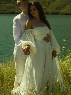 a man and woman standing next to each other in front of a body of water