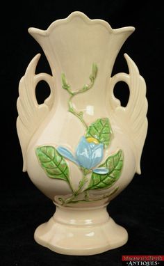 a white vase with a blue flower painted on the side and green leaves around it