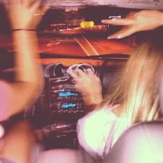 two people driving in a car with their hands on the steering wheel and one person holding an electronic device