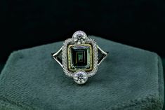 a fancy ring with an emerald surrounded by diamonds on top of a green velvet box