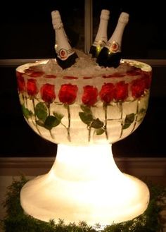 two bottles of champagne sitting on top of a glass bowl filled with ice and roses