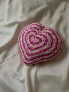 a crocheted heart pillow on a white sheet with pink and white trimmings