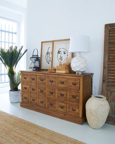 a wooden dresser sitting next to a lamp and potted plant in a living room