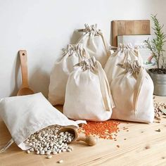 three bags filled with beans sitting on top of a wooden table next to a potted plant