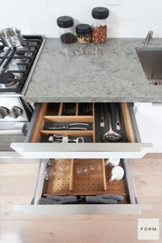 an open drawer with utensils and other kitchen items in the bottom drawer, next to a sink