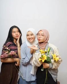 three women standing next to each other with flowers in their hands and one pointing at the camera