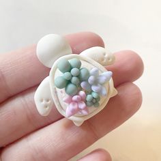 a tiny turtle brooch with pastel colors on it's shell is held in someone's hand