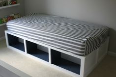 a white bed with striped sheets and blue cubby drawers on the bottom shelf in a child's room