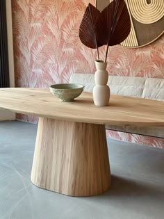 a wooden table with a bowl and vase on it in front of a pink wall