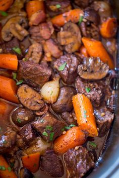 a stew with carrots, mushrooms and meat in a crock pot on the stove