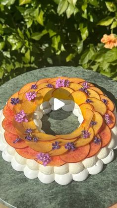 a cake decorated with peaches and flowers on top of a green table in front of some bushes