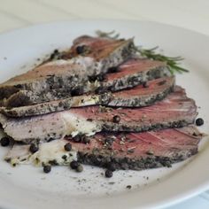 a white plate topped with sliced up meat and garnished with herbs on top